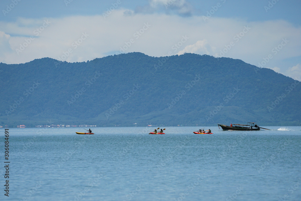 Selective focus on group of travelers canoeing on the surface of sea for touring with seascape and island inbackground