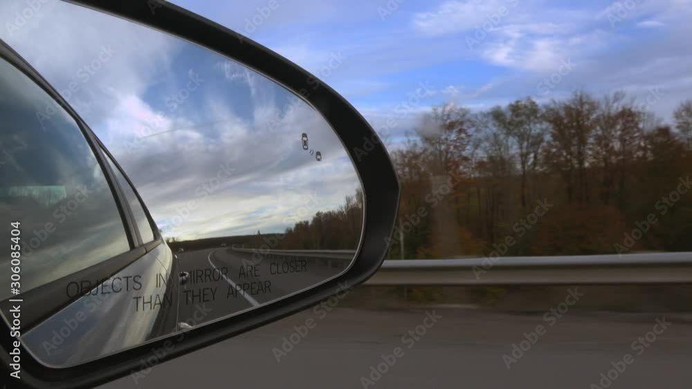 4K. Car mirror while driving on the long road through the beautiful countryside in the United States. North American countryside landscape in autumn with a blue sky with clouds. Traffic concept. 4K. Car mirror while driving on the long road through the beautiful countryside in the United States. North American countryside landscape in autumn with a blue sky with clouds. Traffic concept.