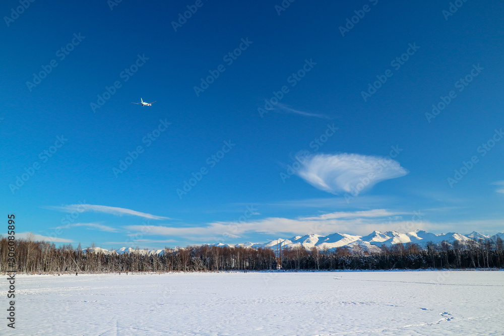 Plane flying south in the winter from Anchorage Airport over dramatic frozen landscape. Concept for winter holiday or vacation and snowbirds