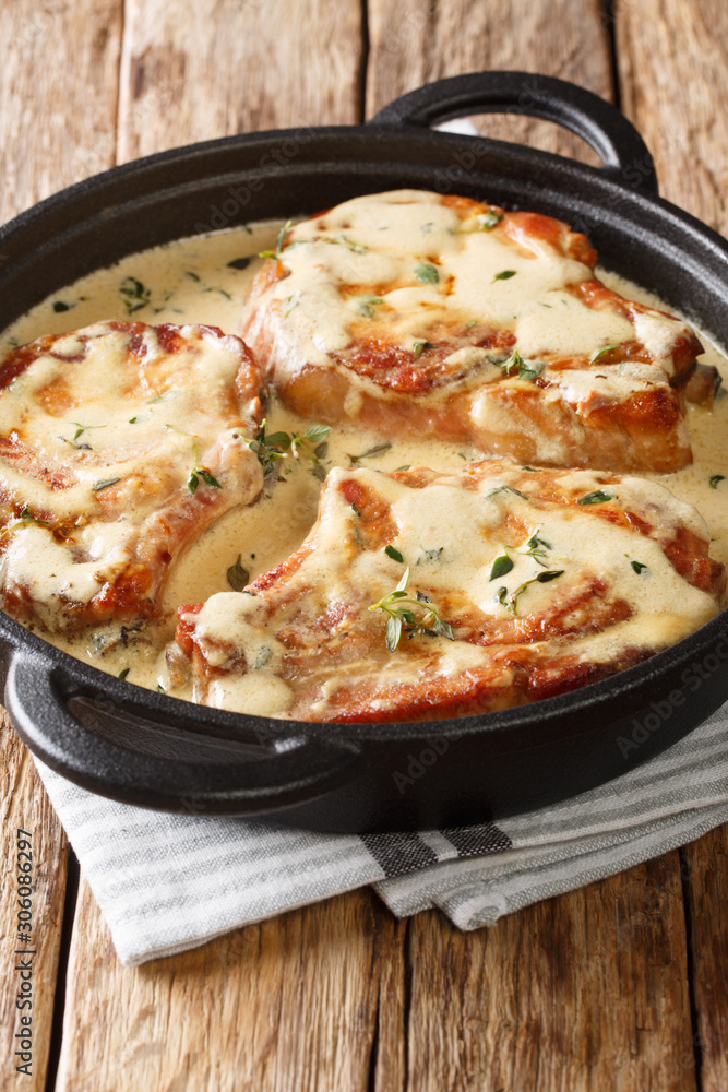 Fried pork chops stewed in a creamy wine sauce with thyme close-up in a pan on the table. vertical Fried pork chops stewed in a creamy wine sauce with thyme close-up in a pan on the table. vertical