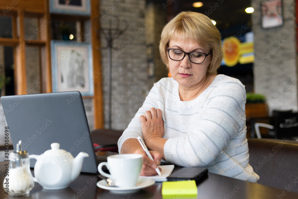 A woman with a laptop looks at a document in a cafe, office A woman with a laptop looks at a document in a cafe, office