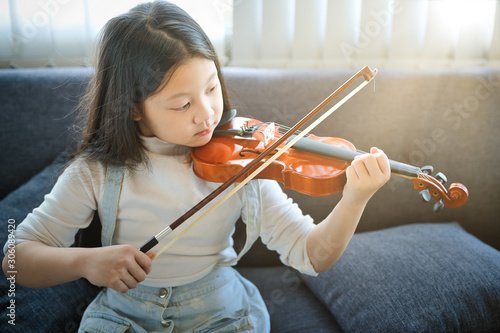 Asian kid learning and practising  to play violin at home