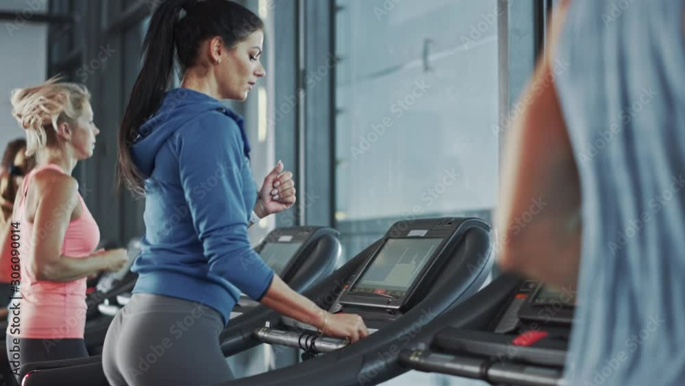 Fit Athletic Woman Running on the Treadmill, Doing Her Fitness Exercise. Muscular Women and Men Actively Training in the Modern Gym. Sports People Workout in Fitness Club. Side View Slow Motion Fit Athletic Woman Running on the Treadmill, Doing Her Fitness Exercise. Muscular Women and Men Actively Training in the Modern Gym. Sports People Workout in Fitness Club. Side View Slow Motion