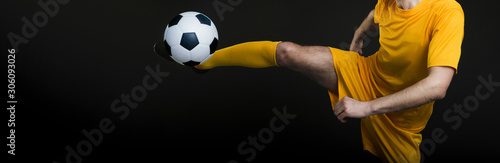 Close up legs and soccer shoe of football player in action kicking ball isolated on black background wearing yellow jersey and sock