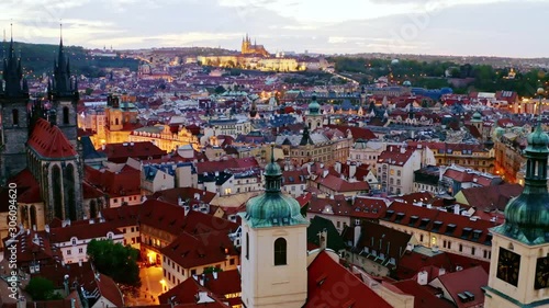 Aerial footage Church of Our Lady and old town district in Prague at twilight. Drone circling near towers and spires moving at low above illuminated streets and buildings with red tiled roof. photo