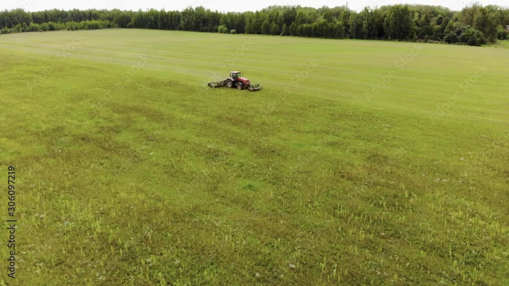 Aerial view of tractor side cutting fresh green grass on silage and haylage on pasture for use as animal feed on farm. The concept of agribusiness Aerial view of tractor side cutting fresh green grass on silage and haylage on pasture for use as animal feed on farm. The concept of agribusiness