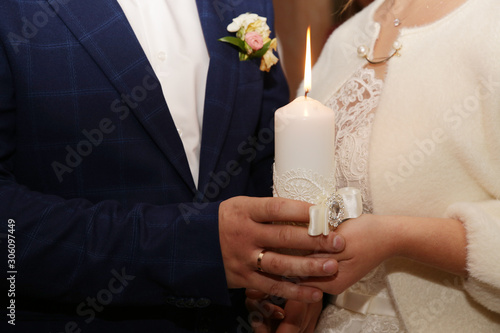 the bride and groom are holding a lit candle, decorated with lace and beads. Hand in hand. Wedding ceremony concept, details.