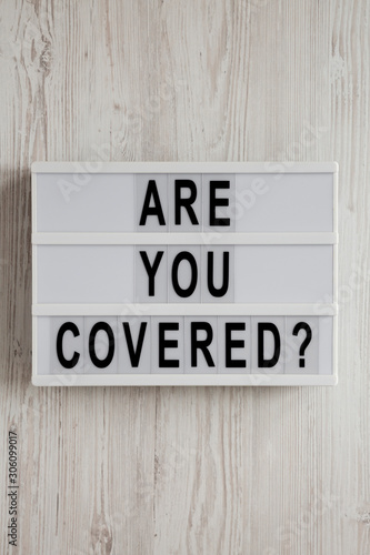 'Are you covered?' words on a modern board on a white wooden surface, top view. Overhead, from above, flat lay. Close-up.
