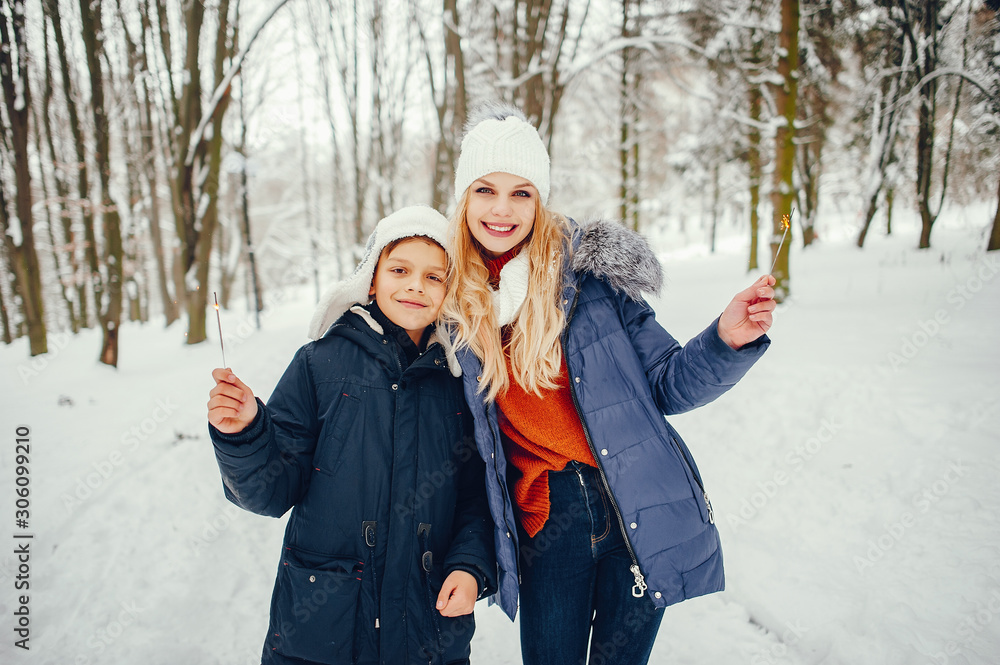 Beautiful mother in a blue jacket. Family playing in a winter park. Little boy in a cute hat Beautiful mother in a blue jacket. Family playing in a winter park. Little boy in a cute hat
