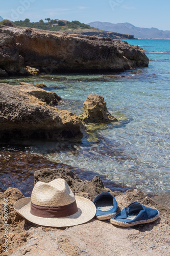Sombrero y sandalias en cala de Mallorca de roca y agua turquesa