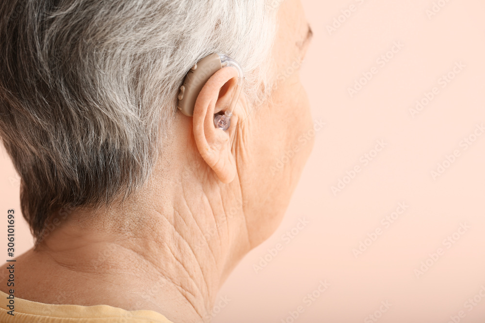 Obraz premium Senior woman with hearing aid on color background, closeup