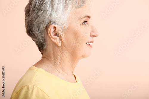 Senior woman with hearing aid on color background