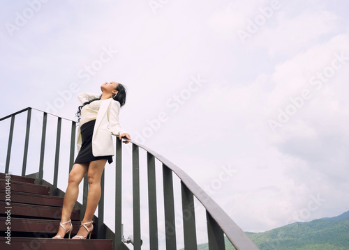 Young Asain beautiful woman standing on stairs feeling freedom face up over sky background, Thailand.
