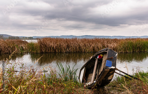 Unused dinghy on the lake, reeds and cloudy sky in the background.