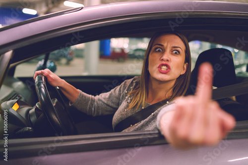Billede på lærred Young woman driver showing middle finger trough the window of the car mad angry