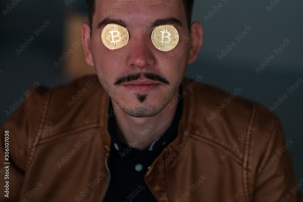 young man with bitcoins in the eye sockets on a dark background. portrait. close-up. emotions young man with bitcoins in the eye sockets on a dark background. portrait. close-up. emotions