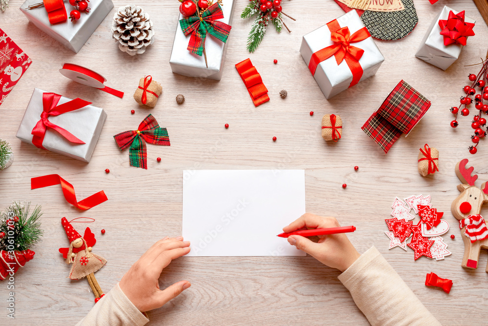 Writing Christmas and New Year greetings. Hand holds pen over blank paper.  Mockup, copy space. Flat lay, top view composition with loats of gifts and  decorations. Stock-Foto | Adobe Stock