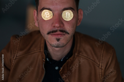 young man with bitcoins in the eye sockets on a dark background. portrait. close-up. emotions