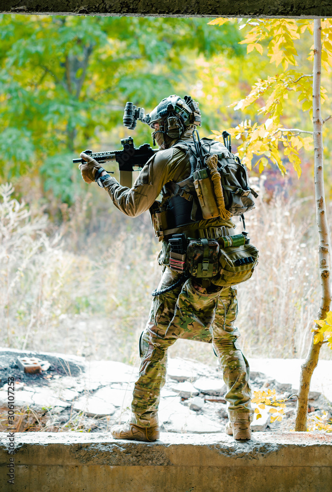 Man in uniform with machine gun on forest background. Airsoft soldier aims at the sight. Vertical photo