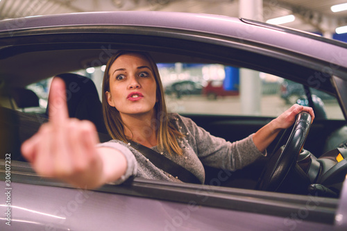 Obraz na plátně Young woman driver showing middle finger trough the window of the car mad angry