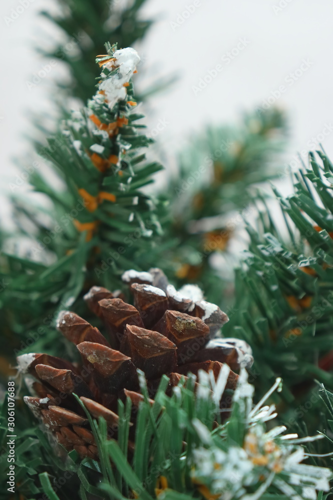 Fototapeta premium Merry christmas and a happy new year! Green Christmas tree lightly dusted with snow. Plastic Christmas tree on a light background with artificial berries and natural pine cones.