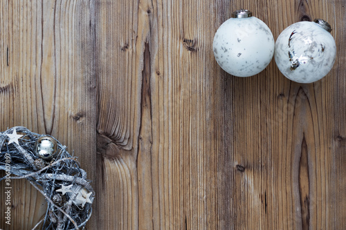 Weihnachtshintergrund mit silbern gefärbter Adventskranz und weißen Christbaumkugeln mit silbernen Applikationen arrangiert auf einem Holztisch