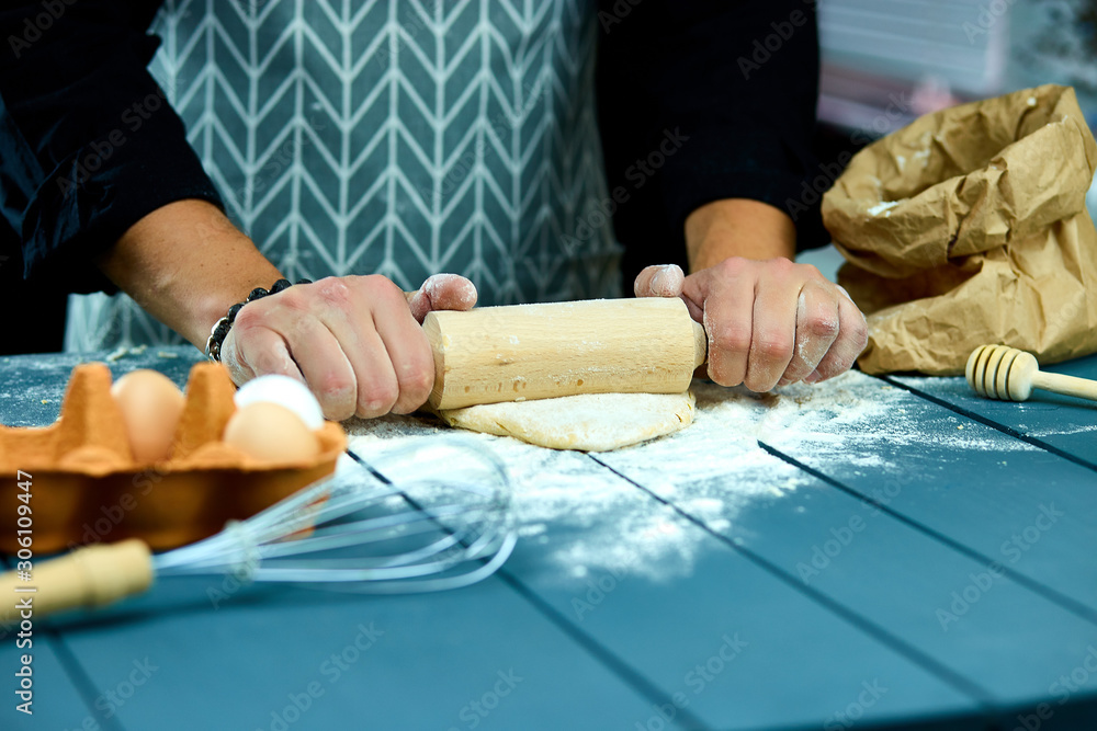 Obraz premium Baker hands preparing fresh dough with rolling pin on kitchen table. Man forming the dough on a floured surface. Cooking pasta, spaghetti, pizza food concept.