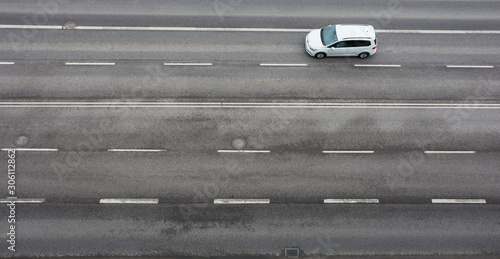 On the road with the asvalt cover, a white car is moving. view from above