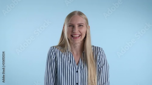 Happy young lady bursting in laughter on blue background. She has long blonde hair.