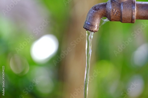 Water flowing from old steel faucet in outdoor space with blur green leaves background for saving water concept