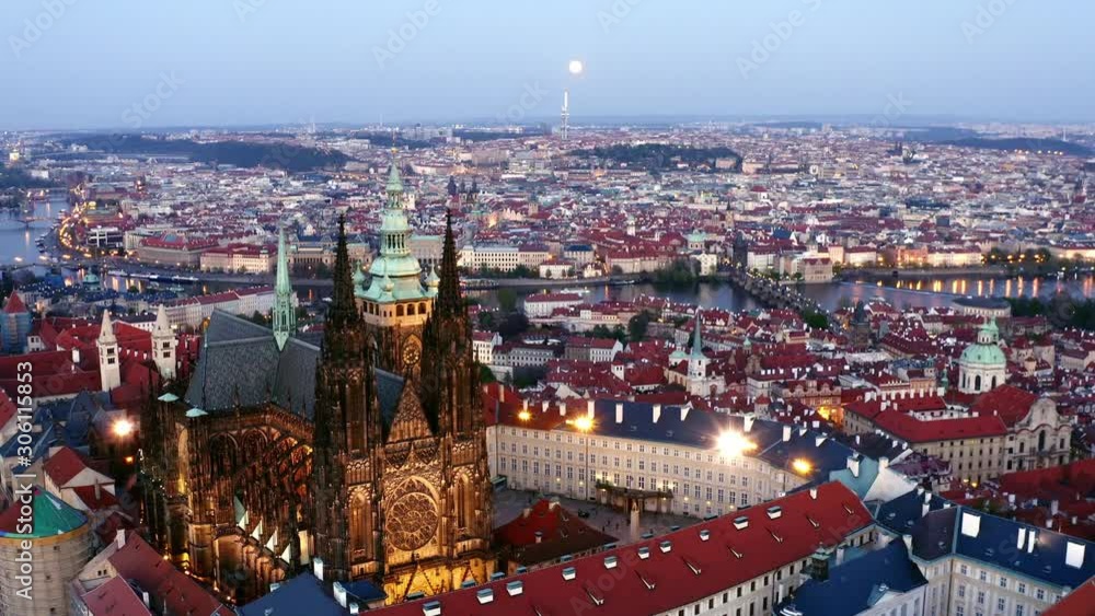 Aerial view of St. Vitus Cathedral in Prague at twilight. Cropped view majestic cathedral, drone flying above buildings with red tiled roof, moving to illuminated towers against picturesque cityscape Aerial view of St. Vitus Cathedral in Prague at twilight. Cropped view majestic cathedral, drone flying above buildings with red tiled roof, moving to illuminated towers against picturesque cityscape