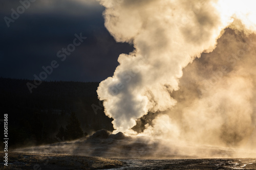 Old Faithful geyser exploded smoke with warm sunlight in early morning.