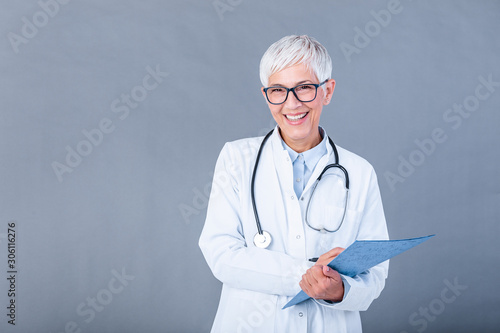 Happy smiling senior female doctor writing on clipboard, isolated on background. Medicine and health care concept. Smiling mature medical doctor woman with stethoscope. photo
