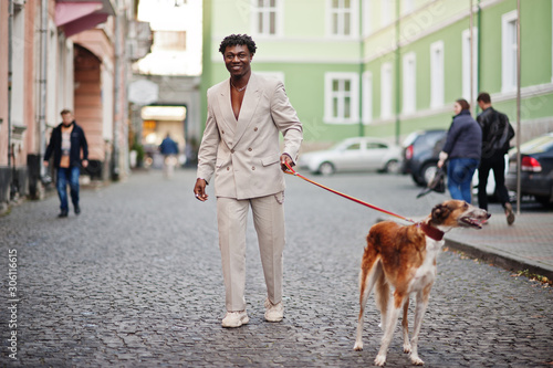 Stylish afro man in beige old school suit with Russian Borzoi dog. Fashionable young African male in casual jacket on bare torso.