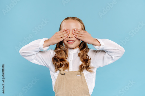 smiling and cute kid obscuring face isolated on blue