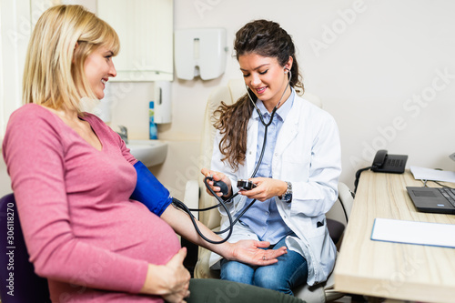 Doctor measuring blood pressure of pregnant woman, gynecology consultation.