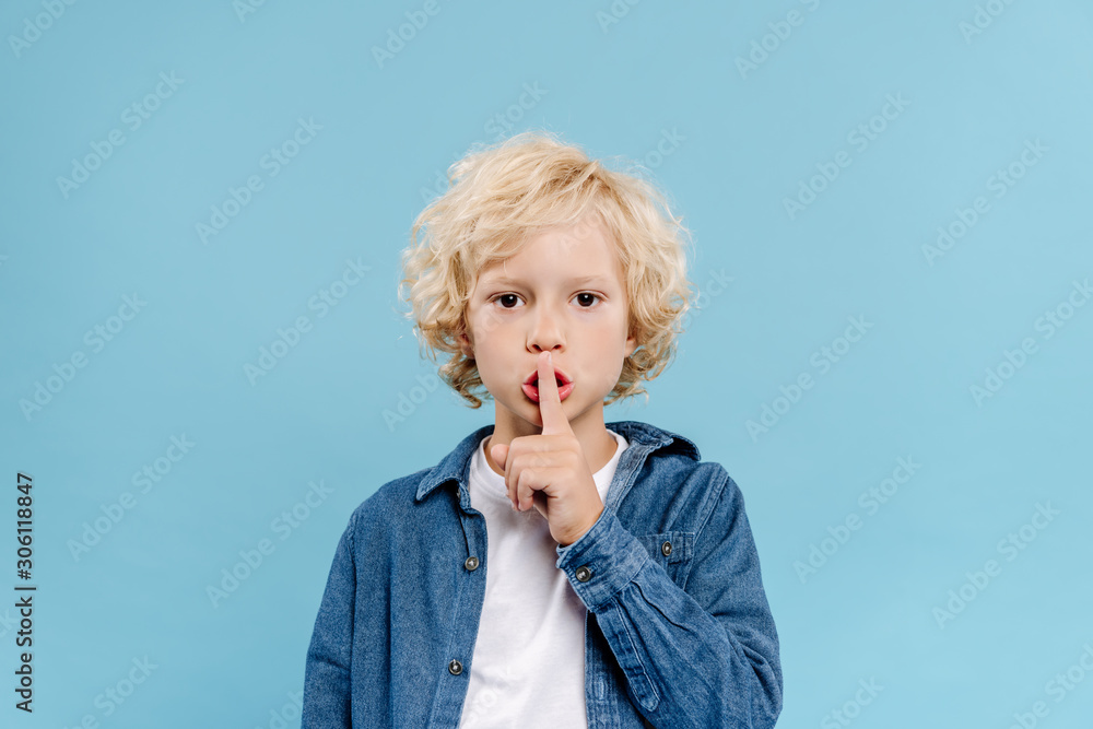 cute kid showing secret gesture and looking at camera isolated on blue - obrazy, fototapety, plakaty 