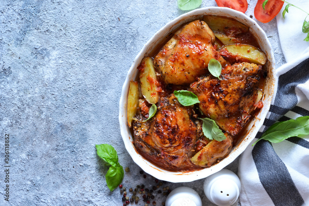 Baked chicken thighs with potatoes, tomato sauce and basil on a concrete background. View from above.