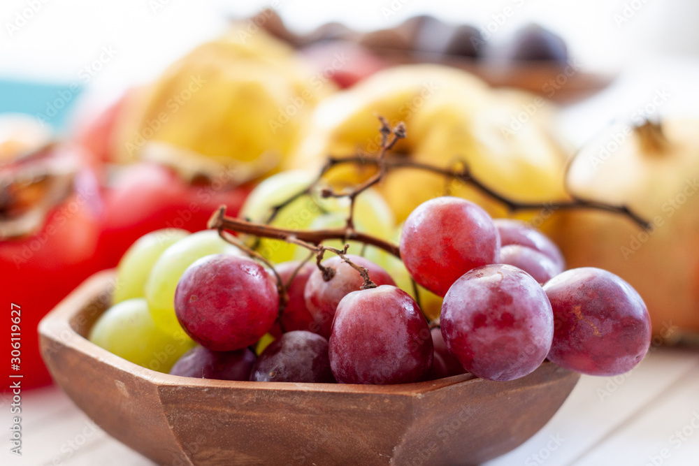 Fall fruits, like grapes, close up over a wooden bowl with a white wooden background with copy space. Fall fruits, like grapes, close up over a wooden bowl with a white wooden background with copy space.