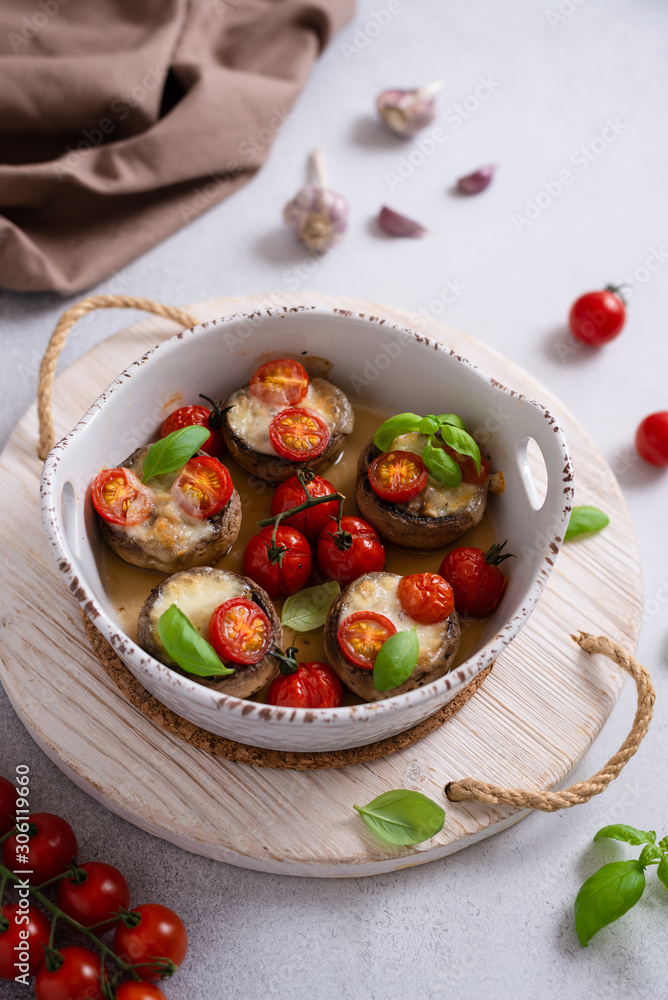Baked Stuffed mushrooms stuffed with mozarella cheese, cherry tomatoes and basil in a casserole dish. Vegetarian dish, ketogenic dieting.
