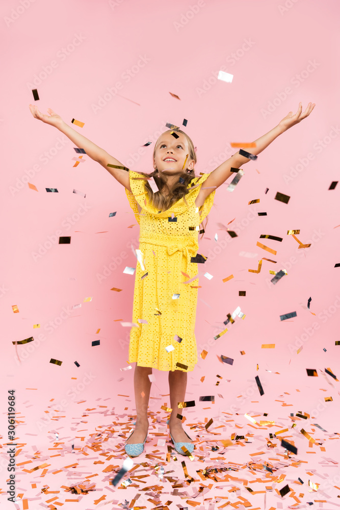 smiling kid with outstretched hands near falling confetti on pink background