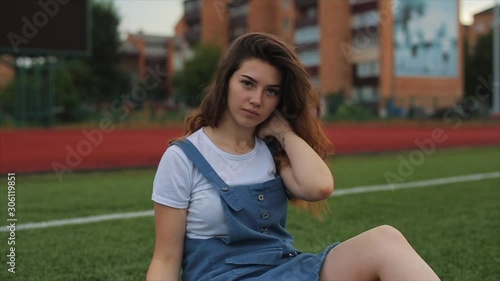 portrait of Beautiful brunette woman inblue sundress sitting on the lawn near a football goal at the stadium. sunlight. A girl with a perfect figure and in great shape. pretty girl in orange photo