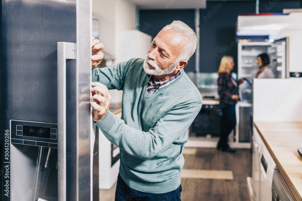Senior bearded customer choosing fridge in appliances store. Senior bearded customer choosing fridge in appliances store.