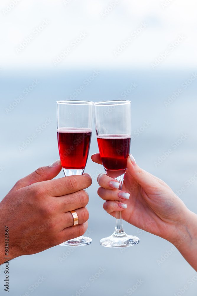 Glasses with red wine in hands on a background of the sea.