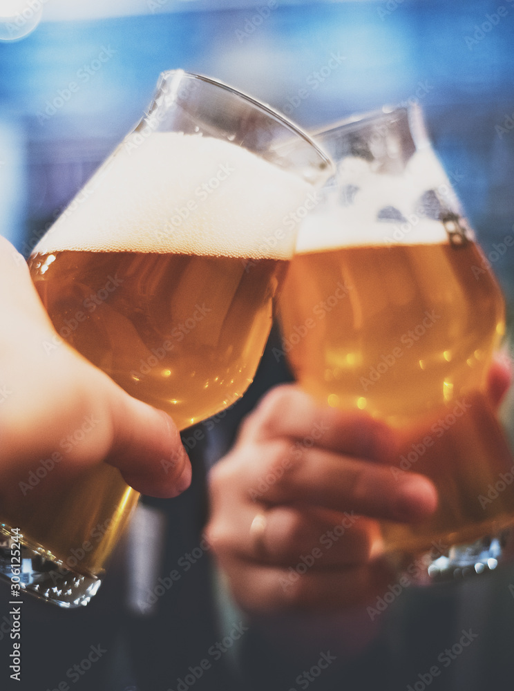 Close-up view of a two glass of beer in hand. Beer glasses clinking in bar or pub Close-up view of a two glass of beer in hand. Beer glasses clinking in bar or pub