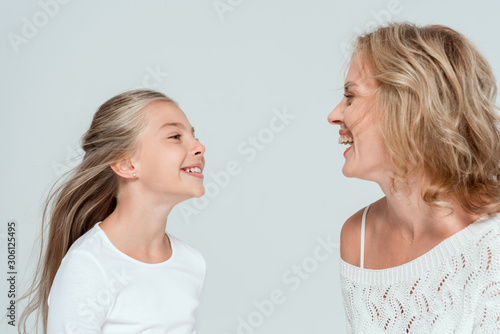 attractive mother and cute daughter smiling and looking at each other isolated on grey