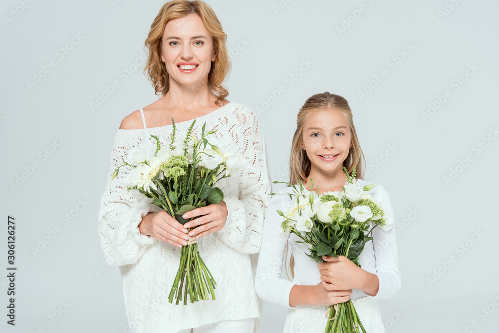 attractive mother and smiling daughter holding bouquets isolated on grey attractive mother and smiling daughter holding bouquets isolated on grey