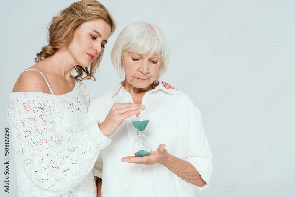attractive daughter hugging and looking with mother at hourglass isolated on grey attractive daughter hugging and looking with mother at hourglass isolated on grey