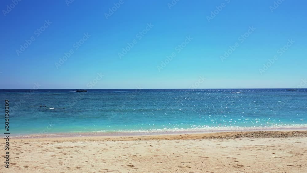 Peaceful seascape with people snorkel into clear blue sea and boats floating around bay, seen from white sandy beach of tropical island on clear blue sky background in Antigua Peaceful seascape with people snorkel into clear blue sea and boats floating around bay, seen from white sandy beach of tropical island on clear blue sky background in Antigua
