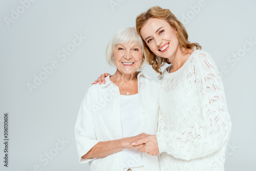 attractive daughter hugging smiling mother and looking at camera isolated on grey